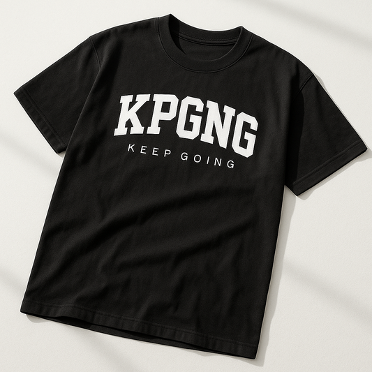 Black t-shirt photographed from an angled top corner on a white surface. Showcases KPGNG logo with 'Keep Going' text, clean shadows, and minimal wrinkles.