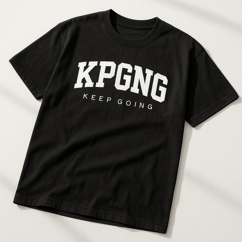 Black t-shirt photographed from an angled top corner on a white surface. Showcases KPGNG logo with 'Keep Going' text, clean shadows, and minimal wrinkles.