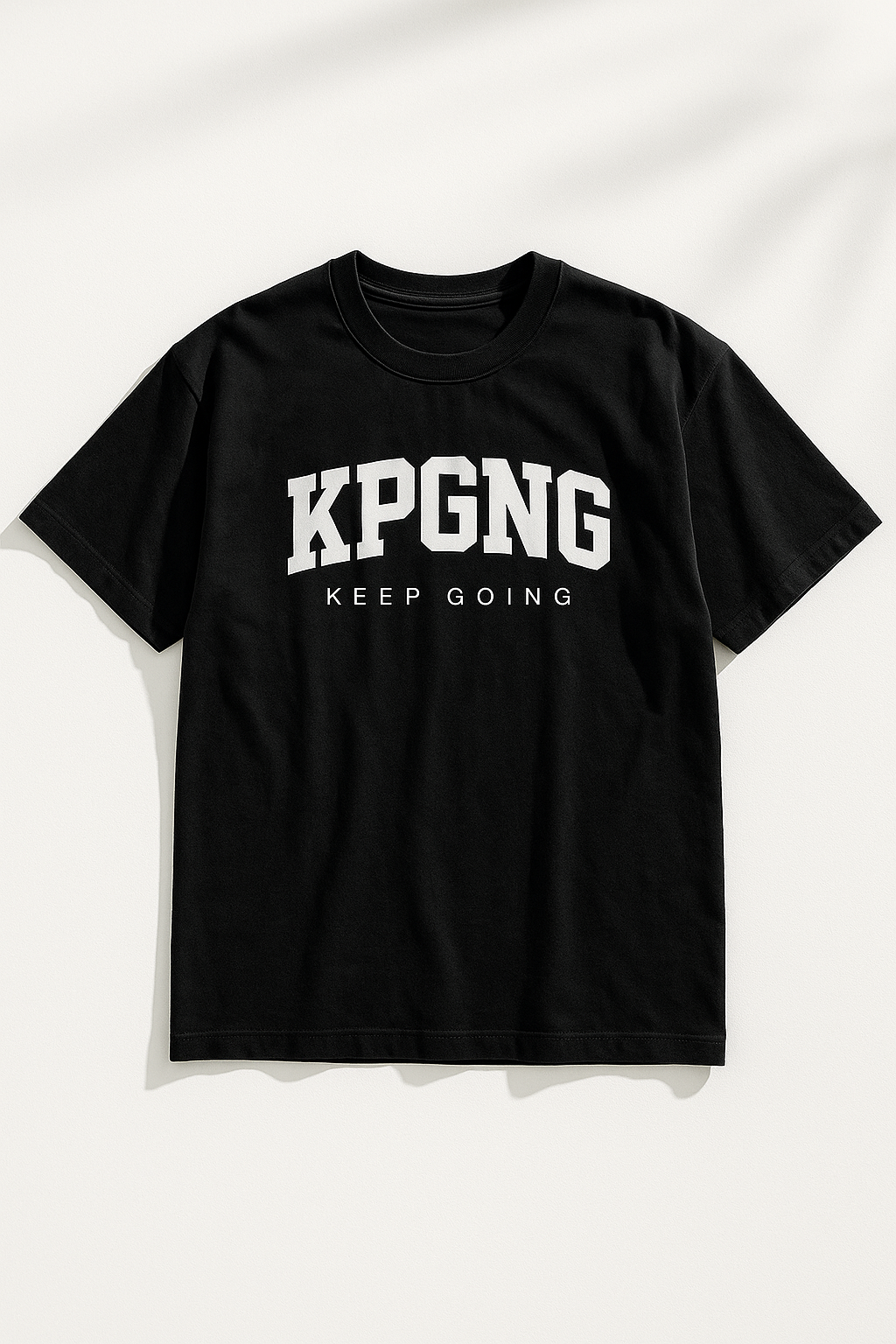 Black t-shirt laid flat on a white background with natural shadows. Features bold KPGNG logo and 'Keep Going' text across the chest.